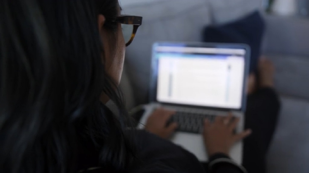Žena sedi na kauču i koristi laptop za čitanje ili pretragu internet sadržaja
