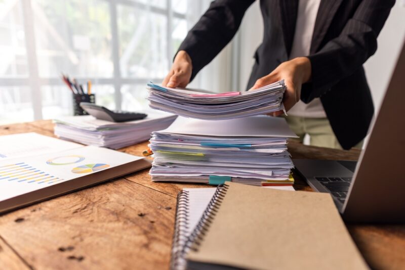 Osoba sortira i slaže dokumenta na radnom stolu uz laptop i kancelarijski materijal